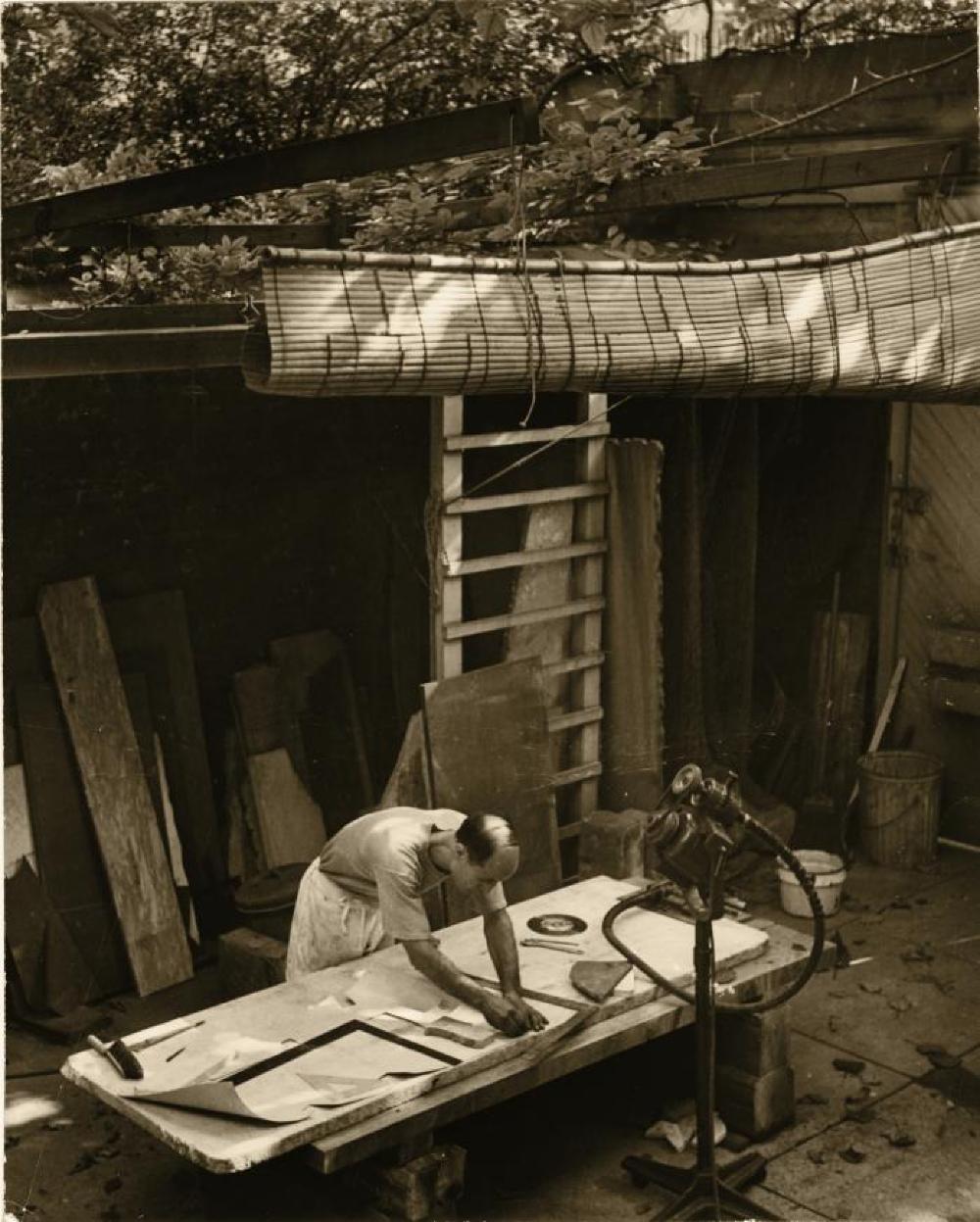Isamu Noguchi working on a marble slab and template in the courtyard of his MacDougal Alley Studio